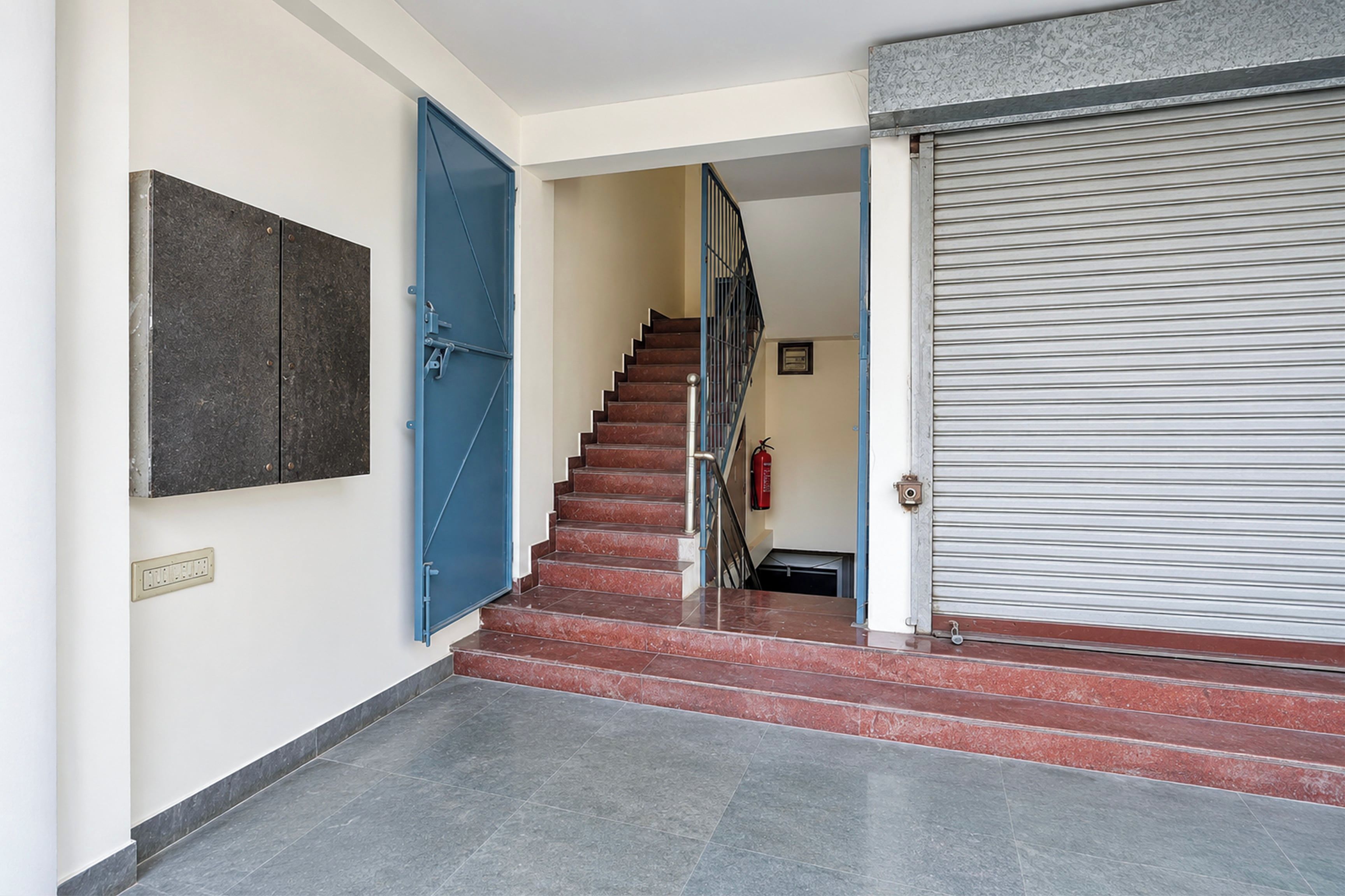 Una escalera con escalones rojos que conduce a una plataforma, una puerta azul a la izquierda y un cerrojo metálico cerrado a la derecha.