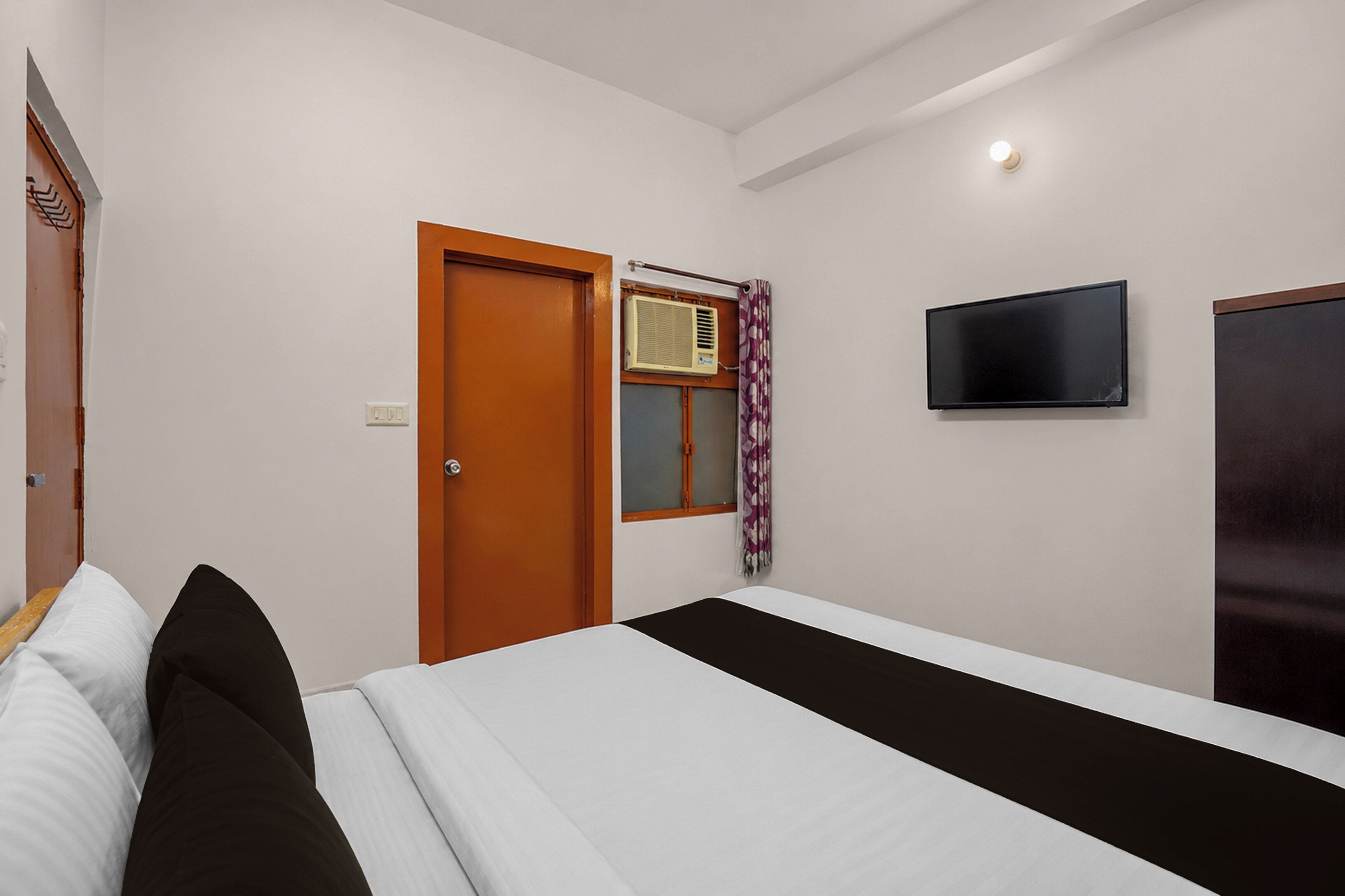 A hotel room with a bed, a television mounted on the wall, and a door with an air conditioning unit.
