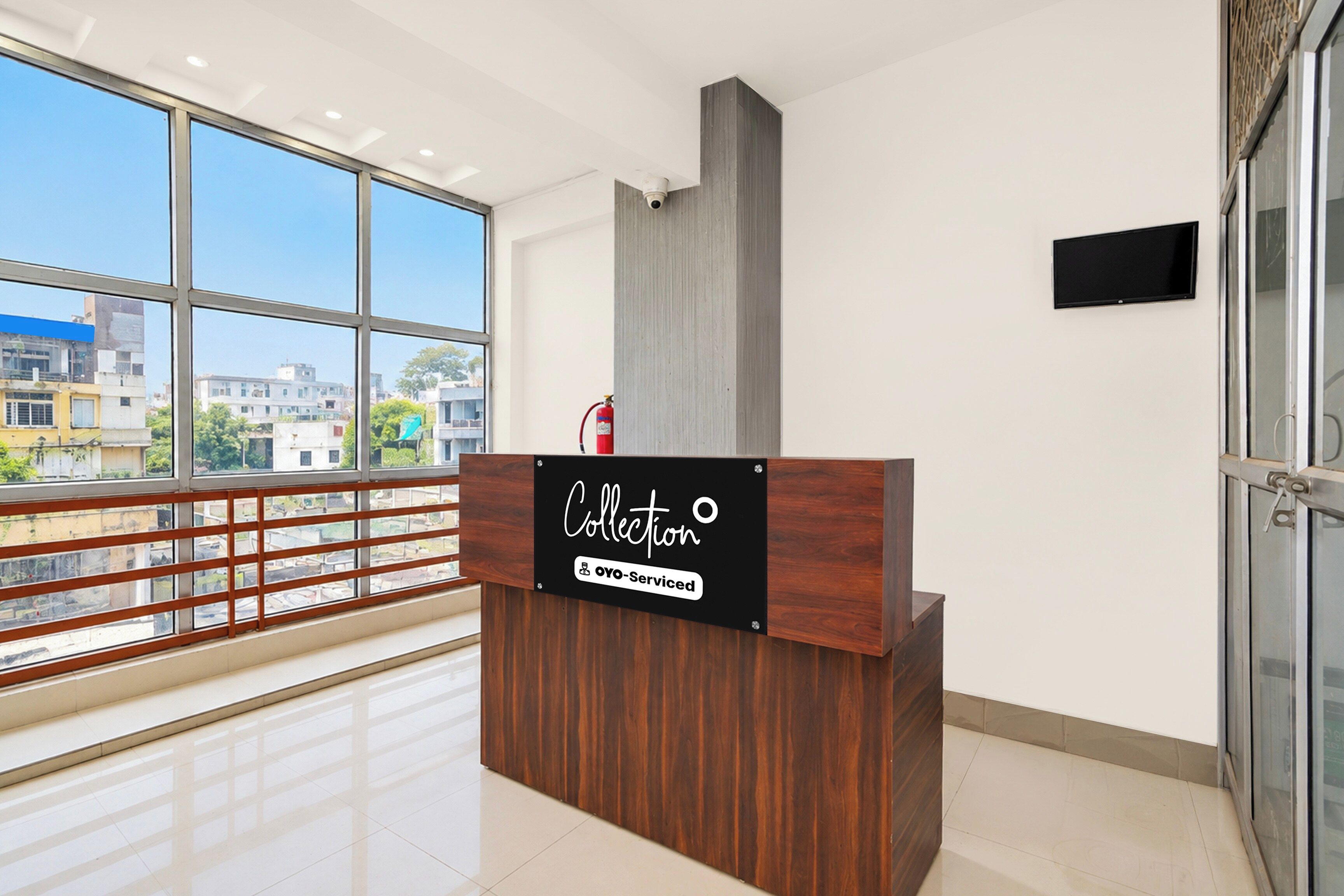 Una recepción con un cartel que indica 'Collection' y 'Oyo-Serviced' en un interior moderno con ventanas amplias y vistas a edificios.