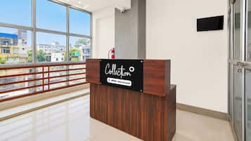Una recepción con un cartel que indica 'Collection' y 'Oyo-Serviced' en un interior moderno con ventanas amplias y vistas a edificios.