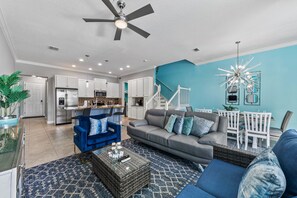 Ein modernes Wohnzimmer mit einem grauen Sofa, einem blauen Sessel und einem Essbereich mit weißen Stühlen.