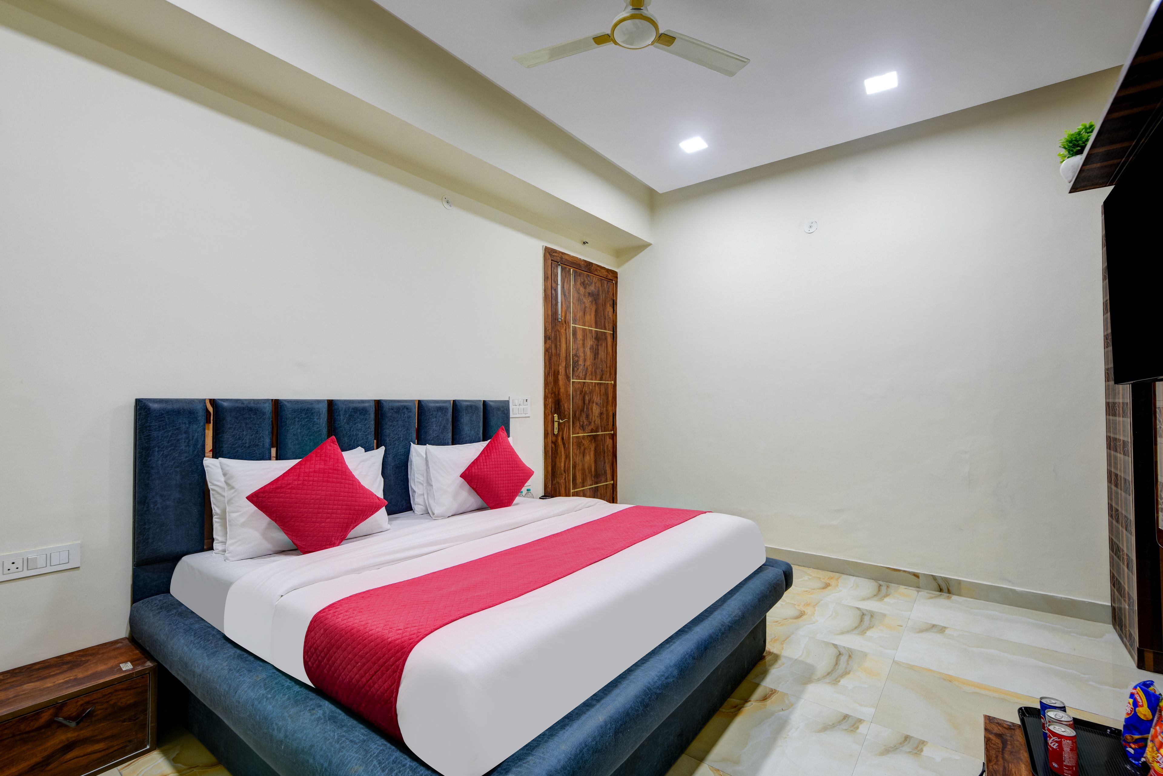 A hotel room with a bed, a wooden door, a ceiling fan, and a marble floor.