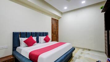 A hotel room with a bed, a wooden door, a ceiling fan, and a marble floor.