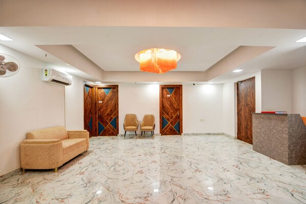 A hotel lobby with a marble floor, a sofa, two chairs, a reception desk, and a decorative ceiling light.