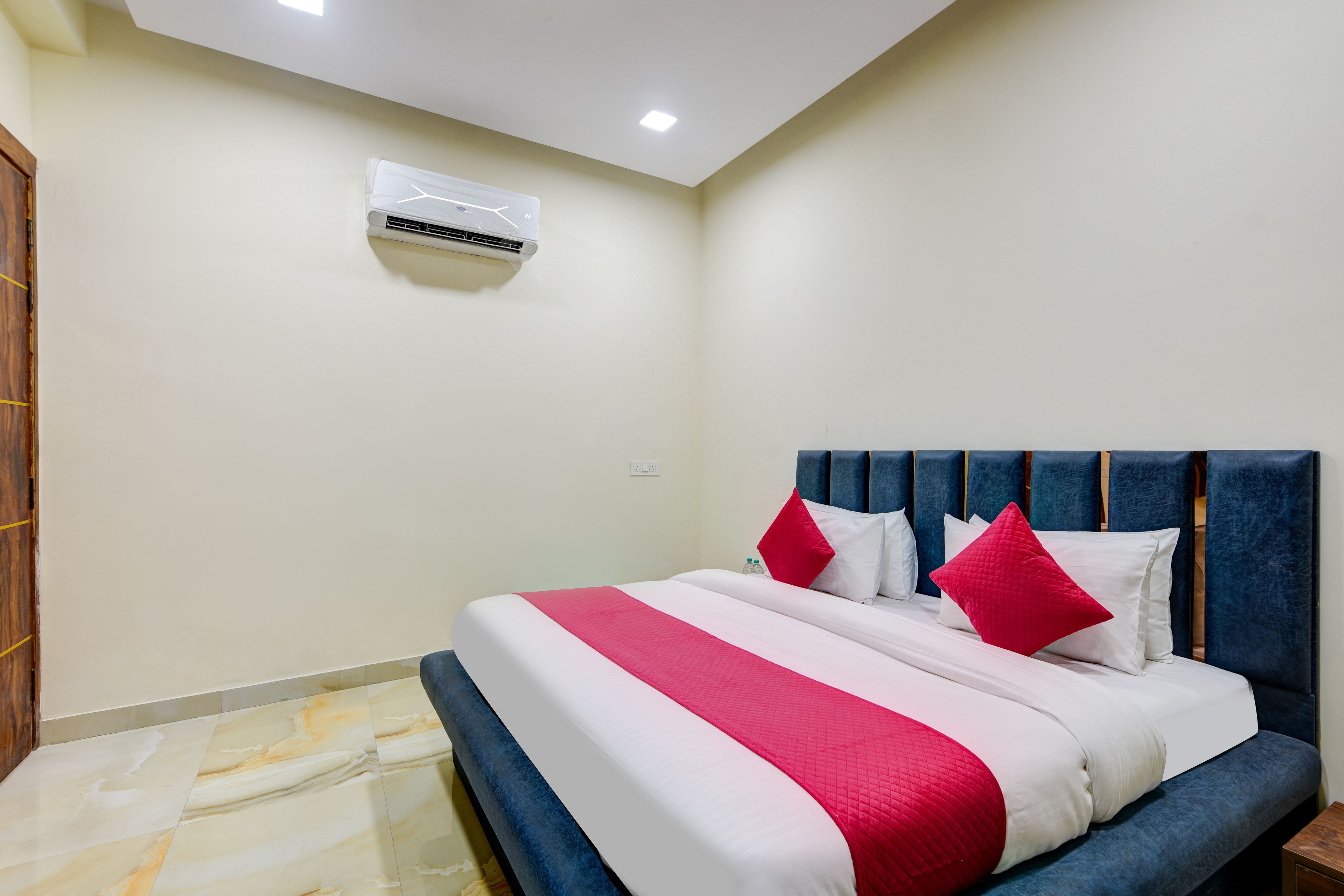 A hotel room with a bed, a headboard, an air conditioning unit, and a tiled floor.