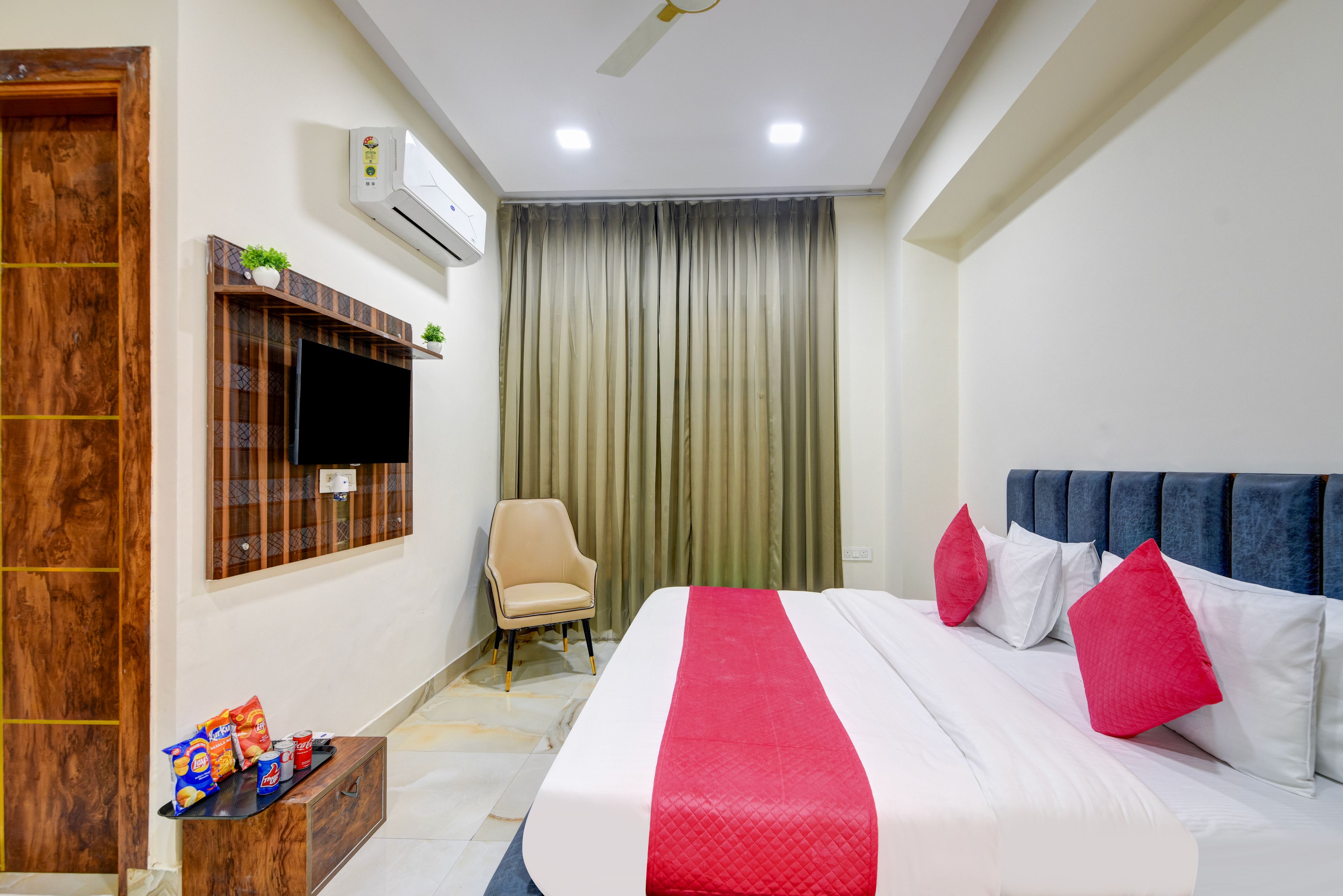 Habitación de hotel con cama, televisión, aire acondicionado, una silla y una mesita con aperitivos.