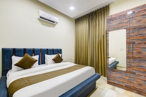 A hotel room with a bed, an air conditioning unit, a mirror, and a curtain.