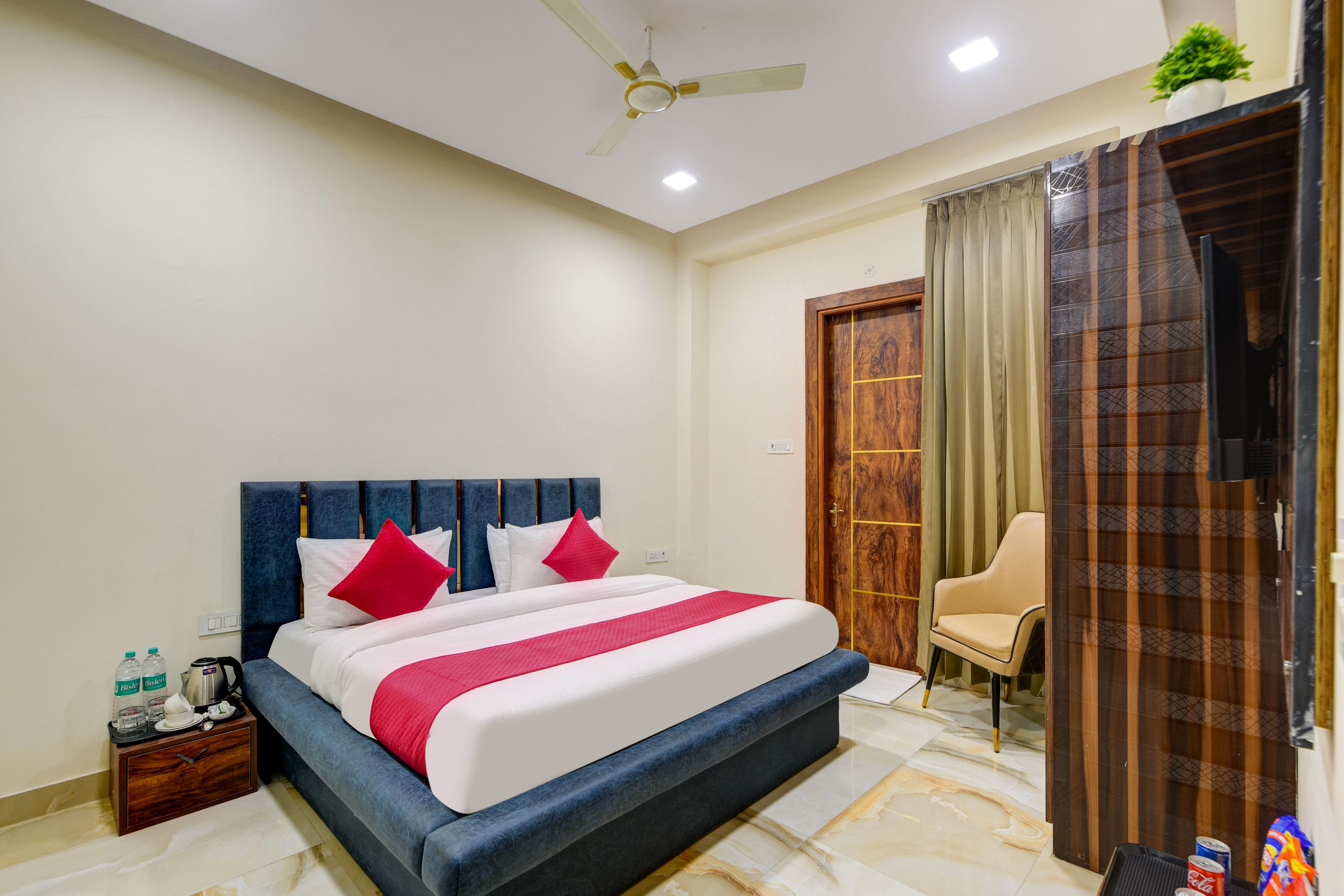 A hotel room with a bed, a chair, a wooden door, and a ceiling fan.