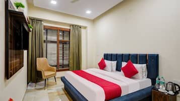 Habitación de hotel con cama, una silla, un escritorio con hervidor y ventana con cortinas.