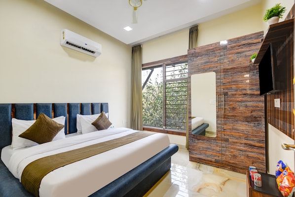 A modern hotel room with a large bed, a built-in air conditioner, a bathroom with a mirror, and a view of greenery outside.