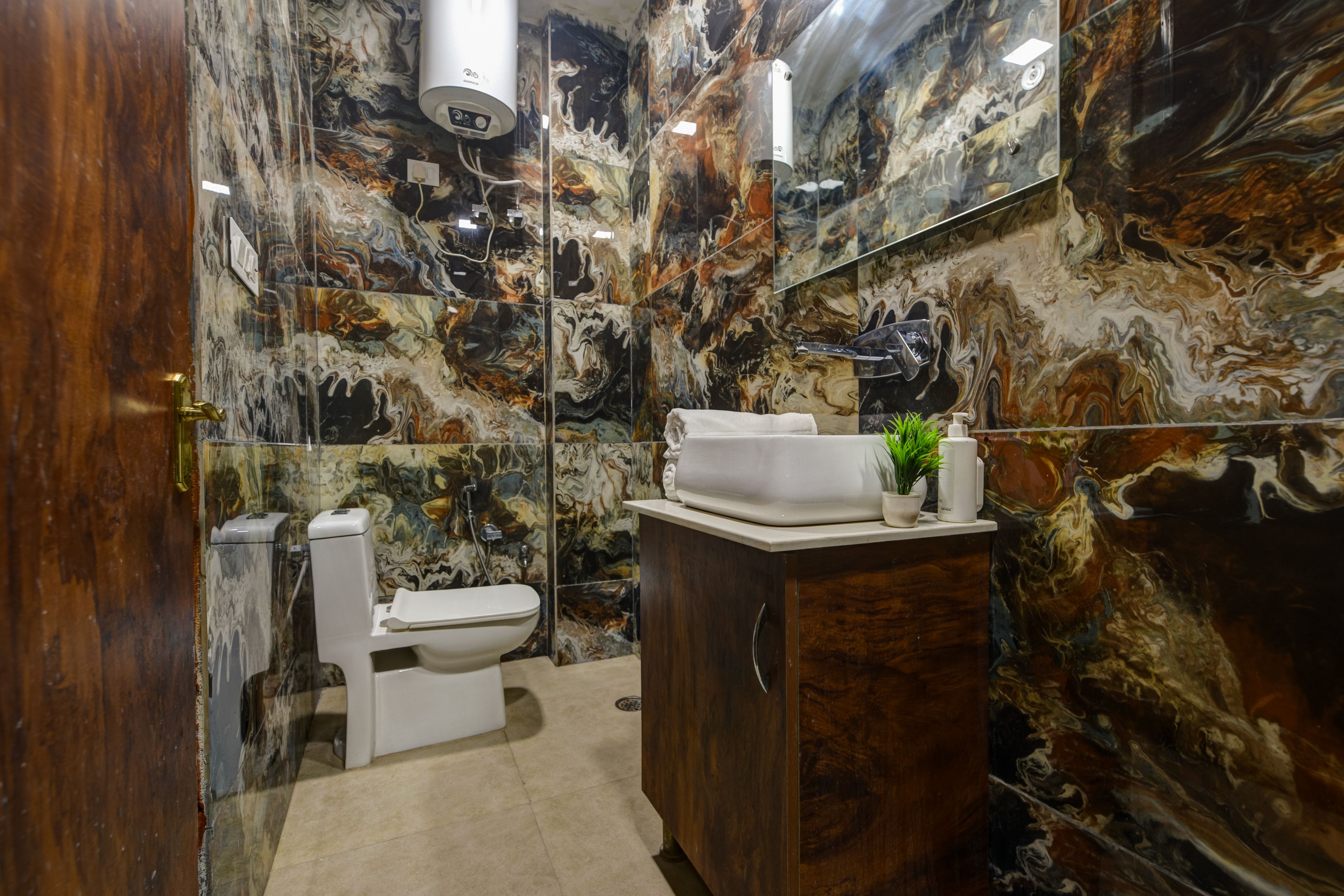 Un baño con pared de mármol, inodoro blanco, lavamanos con espejo y un armario.