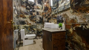 Un baño con pared de mármol, inodoro blanco, lavamanos con espejo y un armario.