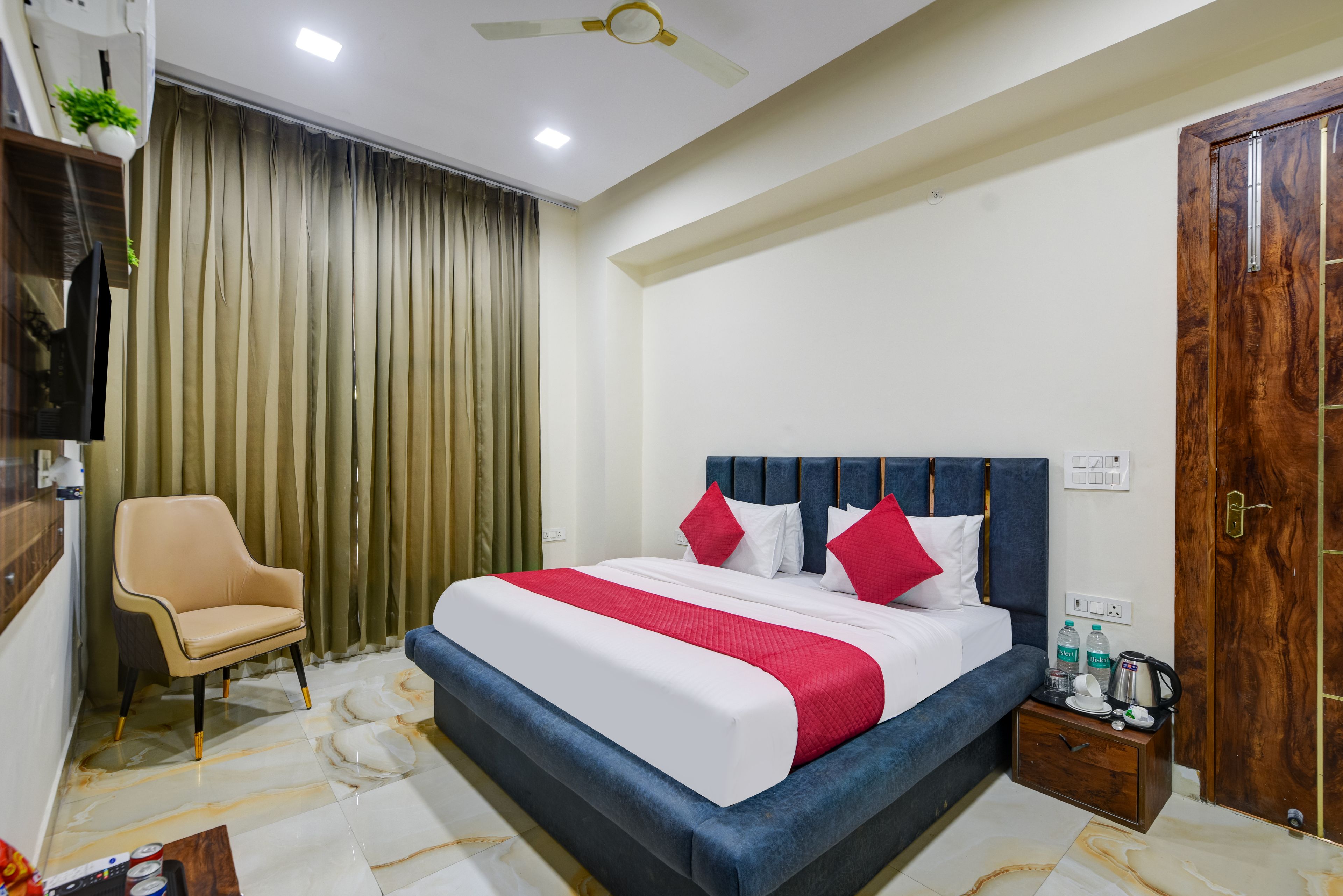 Una habitación de hotel con una cama, una silla, una puerta de madera y un ventilador de techo.