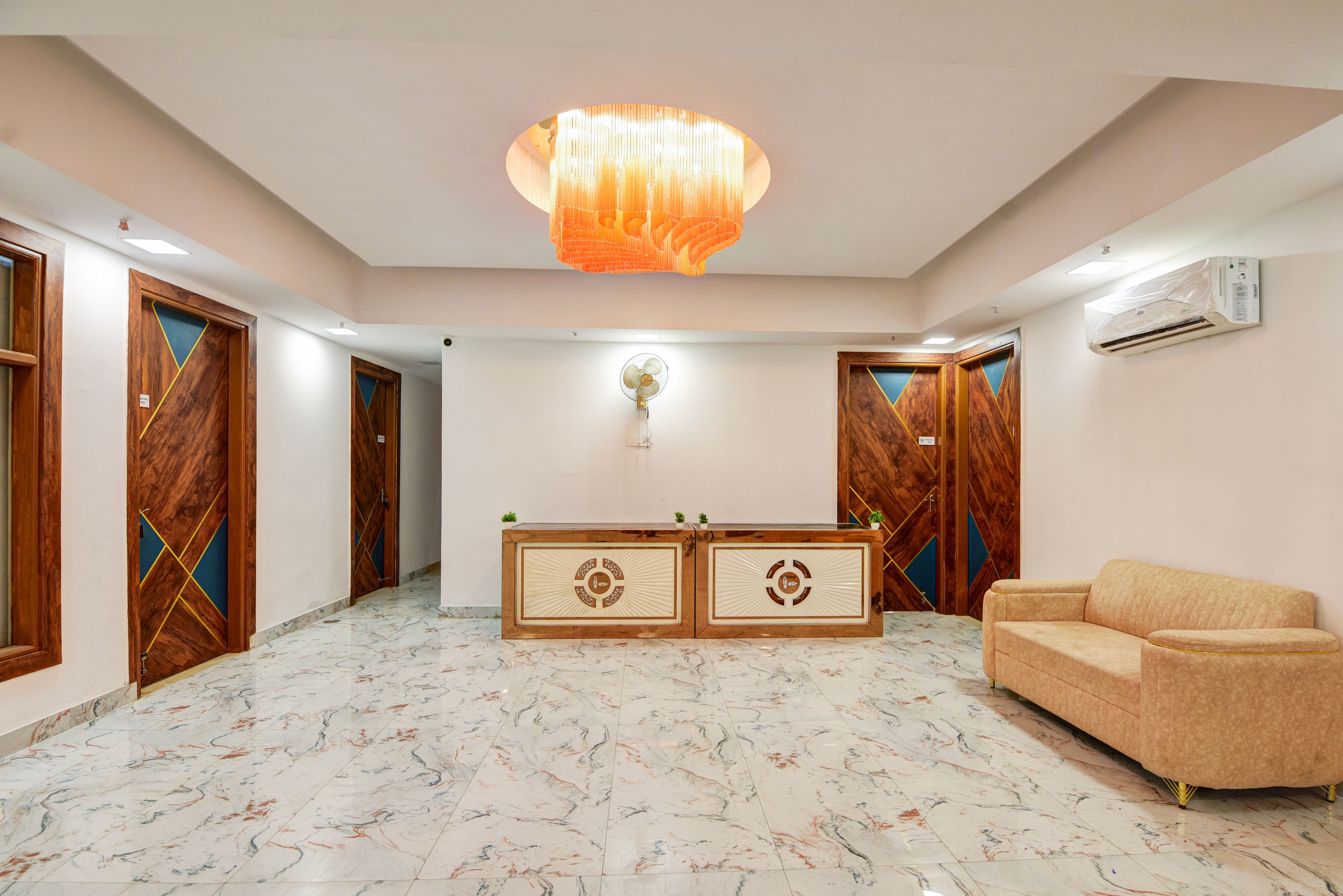 Un vestíbulo de hotel con pisos de mármol, una recepción, un sofá y puertas de madera con diseños geométricos.