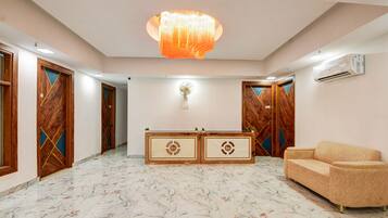 Un vestíbulo de hotel con pisos de mármol, una recepción, un sofá y puertas de madera con diseños geométricos.