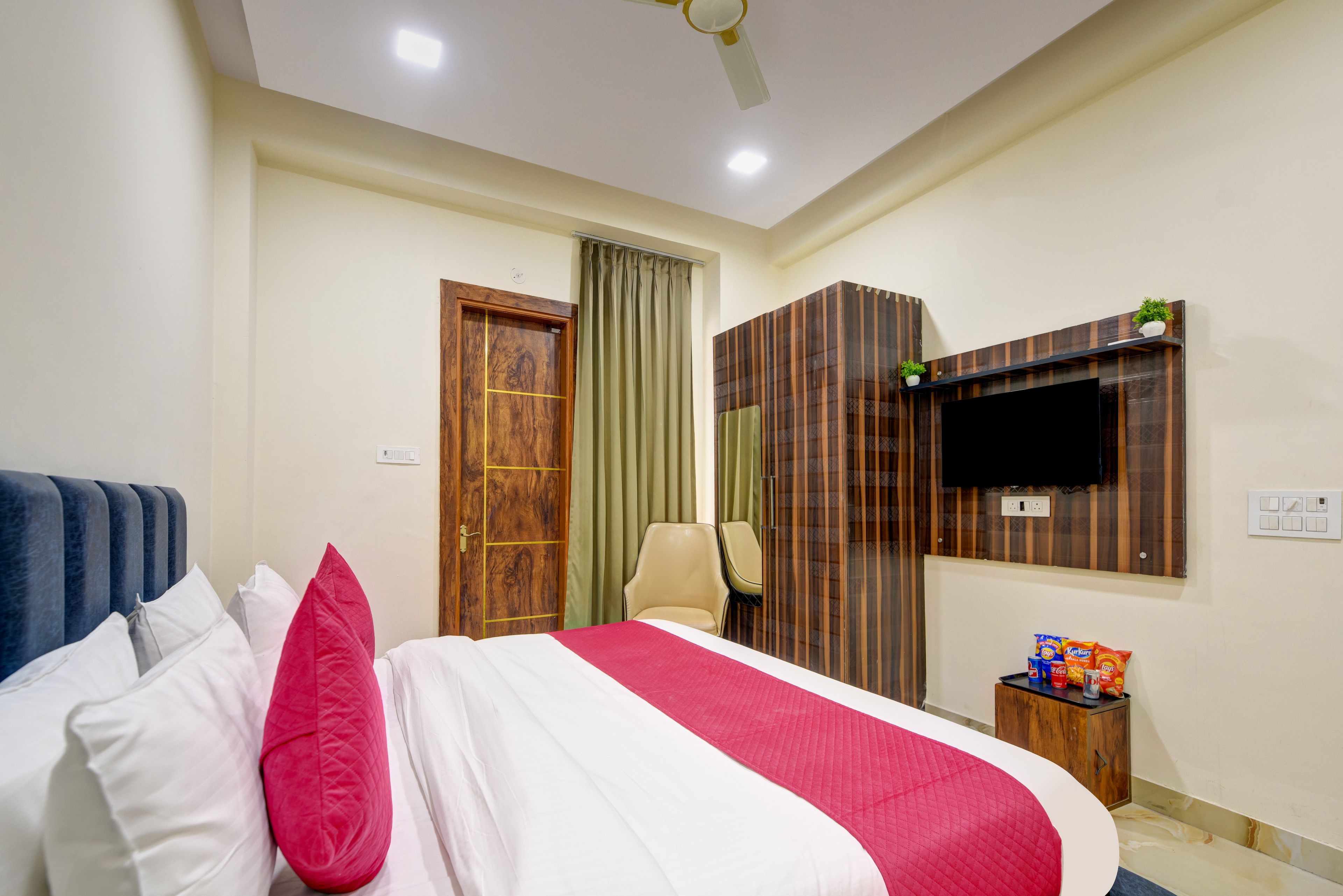 Habitación de hotel con cama, televisión montada en la pared, un mueble pequeño y ventilador de techo.