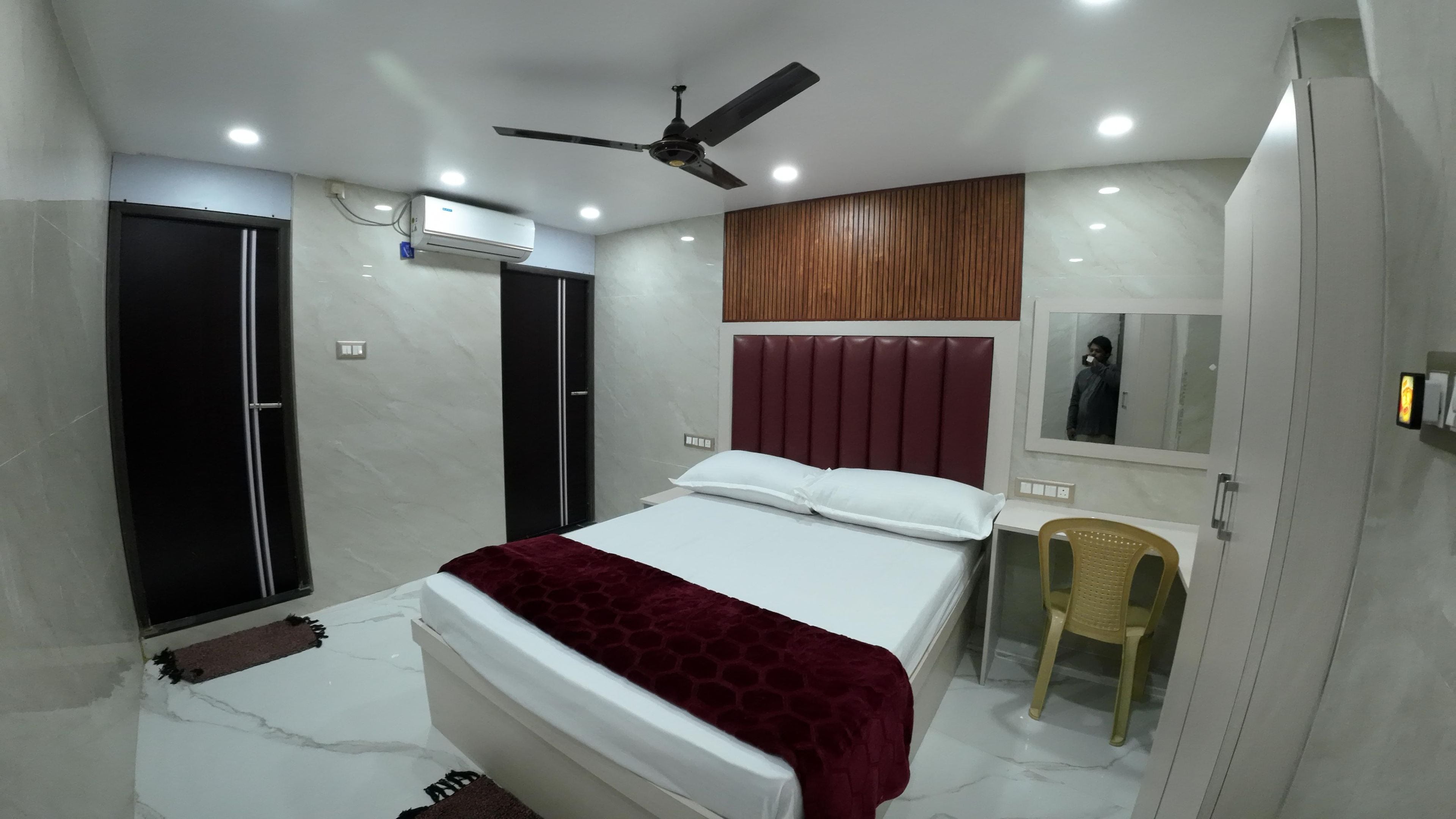 A bedroom with a bed, a ceiling fan, a wardrobe, a mirror, and a chair.