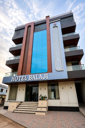 A hotel named 'HOTEL BALAJI' with a modern facade, multiple balconies, and a prominent blue glass window.