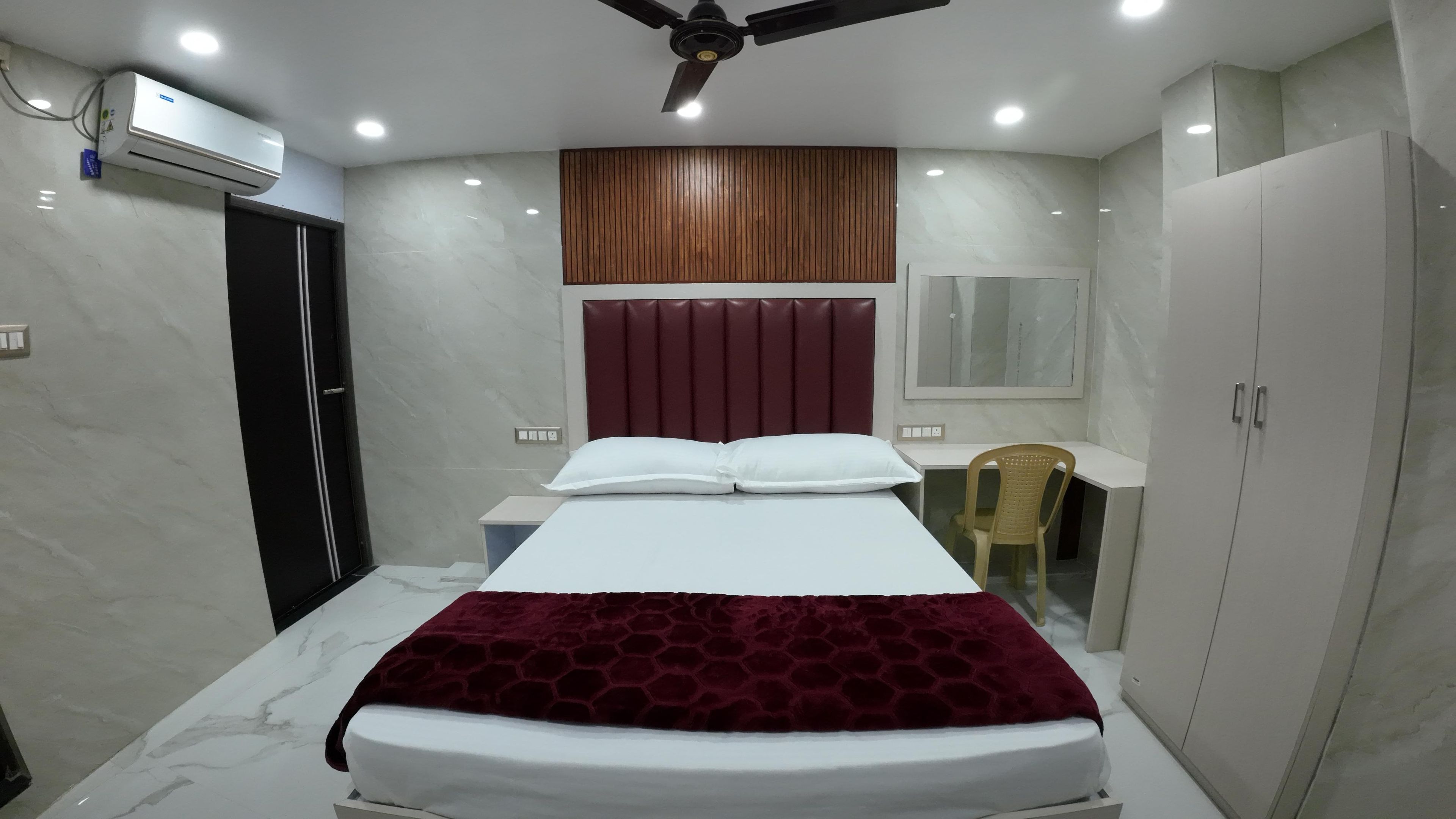 A bedroom with a bed, a desk, a chair, a wardrobe, a ceiling fan, and an air conditioning unit.