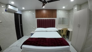 A bedroom with a bed, a desk, a chair, a wardrobe, a ceiling fan, and an air conditioning unit.