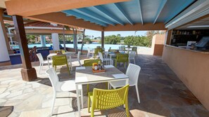 Un patio al aire libre con mesas y sillas, una piscina al fondo y una barra.