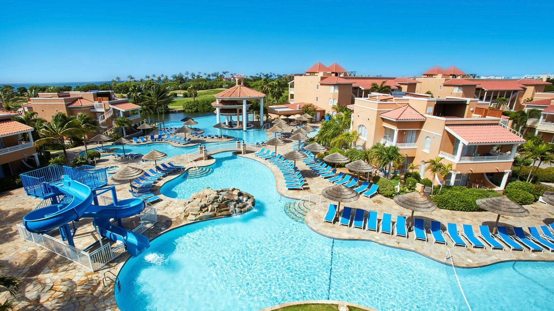 Een resort met een groot zwembad, verschillende ontspanningsruimtes en uitzicht op de oceaan.