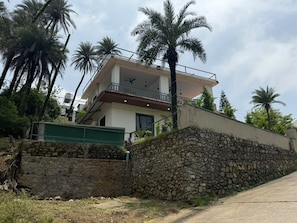 A two-story building with a balcony, surrounded by palm trees and a stone wall.