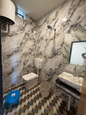 Een badkamer met marmeren wanden, een toilet, een wastafel en een douche.