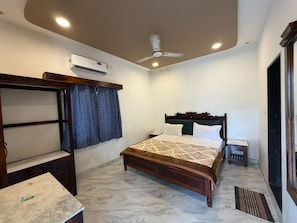 A bedroom with a bed, a bedside table, a nightstand, an air conditioning unit, a ceiling fan, and a window with curtains.