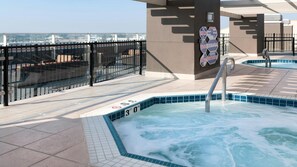 Poolområde på taget med jacuzzi, glasgelænder og udsigt over bybilledet.