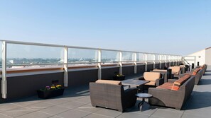 En tagterrasse med udendørs siddepladser, udsigt over byen og en klar himmel.
