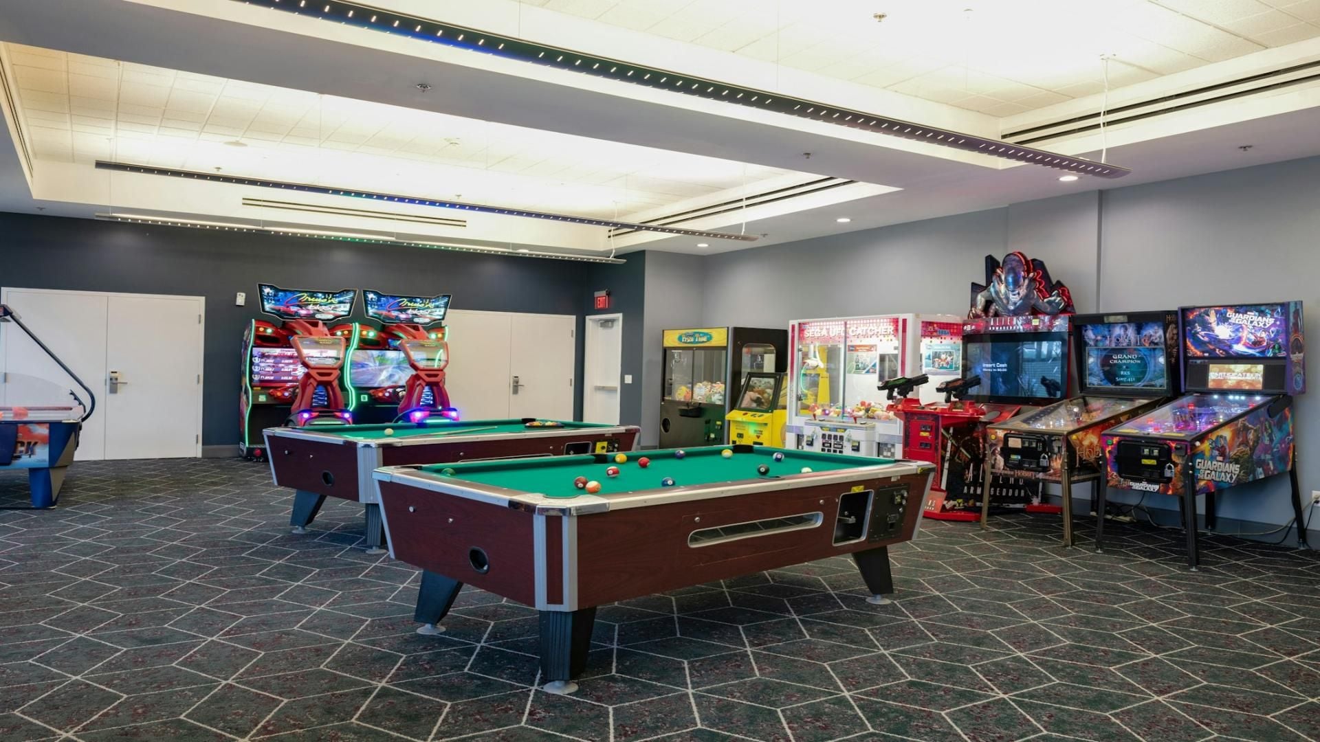 A pool table with a billiards cue, a pool table, and a video game arcade with various games.