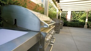 En grill med flad grillrist og et udluftningsgab, placeret under en pergola med udsigt til grønne områder.