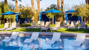 Un espace piscine doté de chaises longues et de parasols, entouré d’arbres et surplombé d’un ciel dégagé.