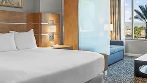 A hotel room with a large bed, a nightstand with a lamp, a seating area with a sofa, and a view of the outdoors. - Club Wyndham Desert Blue - Studio, Free Shuttle to the Strip (Las Vegas)