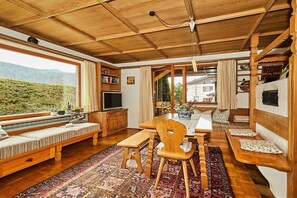 Ein gemütliches Interieur mit Holzbalkendecke, einer Essecke mit Tisch und Stühlen, einem Sofa und einem Fernseher.