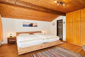 Ein Schlafzimmer mit Holzboden, einem Bett mit weißer Bettwäsche, einem Nachttisch mit Lampe und einem farbenfrohen StreifenTeppich.