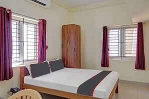 A bedroom with a bed, a wardrobe, and two windows with curtains.