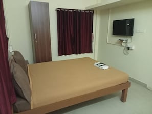 Ein Zimmer mit einem Bett, einem Schrank, einem an der Wand befestigten Fernseher und einem Vorhang.