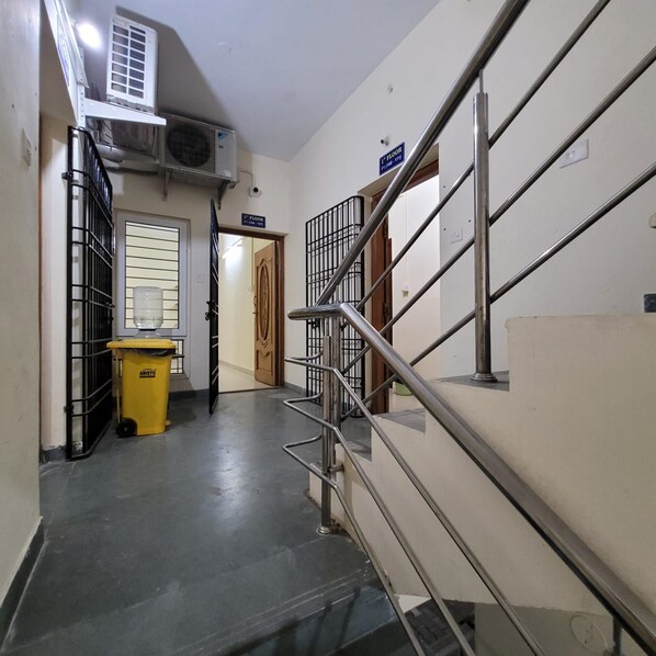 A corridor with a staircase leading to the first floor, a trash bin, and an air conditioning unit on the wall.
