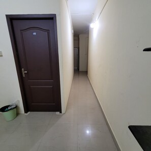 A hallway with a closed door, a trash bin, and a light fixture on the wall.