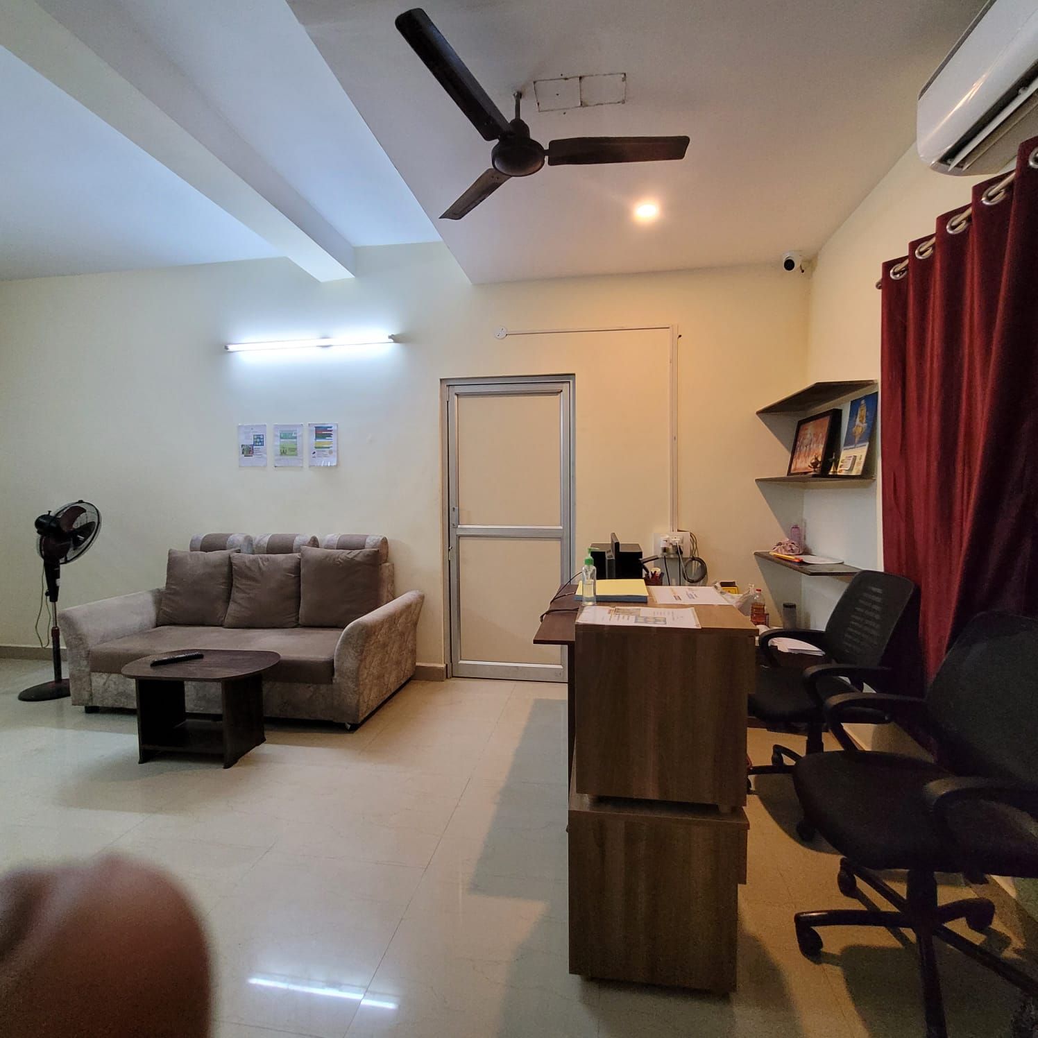 Un salon comprenant un canapé, une table basse, un bureau avec une chaise, un ventilateur de plafond et une porte.