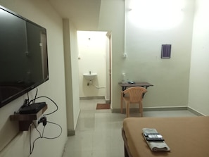 Une chambre d’hôtel avec un lit, un bureau, une chaise, une télévision et, au fond, une salle de bain.