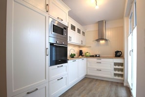 A modern kitchen with white cabinetry, stainless steel appliances, and a built-in range hood. - Holiday apartment with 2 bedrooms (Norderney)