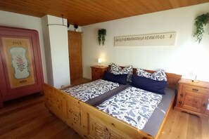 Ein hölzernes Bett mit gemusterten Betttextilien, ein Nachttisch, eine Wandlampe und ein gerahmtes Bild.