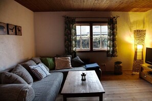 A cozy living room with a sofa, a coffee table, a TV, and a window with curtains. - Cottage by the reeds (Farchant)
