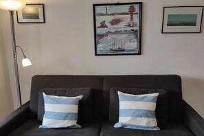 A dark-colored sofa with two pillows, a floor lamp, and two framed pictures on the wall. - Iderhoff Apartment 53 (Norderney)