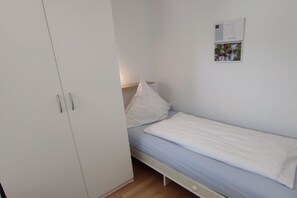 A small, single-bed room with a white wardrobe and a wall-mounted calendar. - Iderhoff Apartment 53 (Norderney)