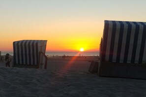 A beach with striped beach umbrellas and a sunset in the background. - Iderhoff Apartment 53 (Norderney)