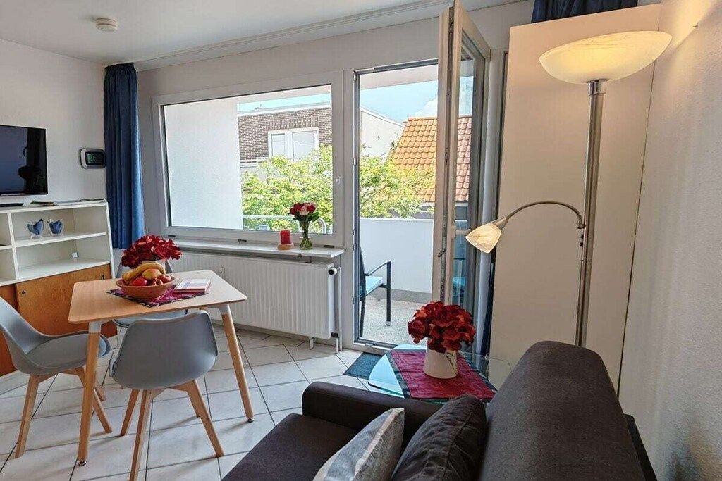 Een moderne woonkamer met een bank, een eettafel met stoelen, een televisie en een raam met uitzicht op een gebouw en bomen.